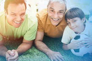 Hispanic grandfather, father and son laying in grass
